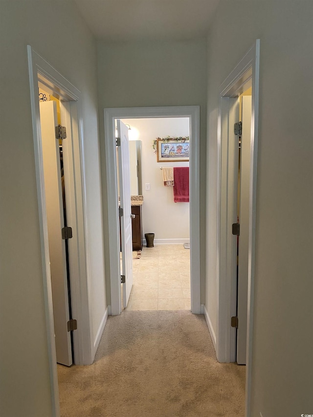 corridor with light colored carpet, baseboards, and light tile patterned floors