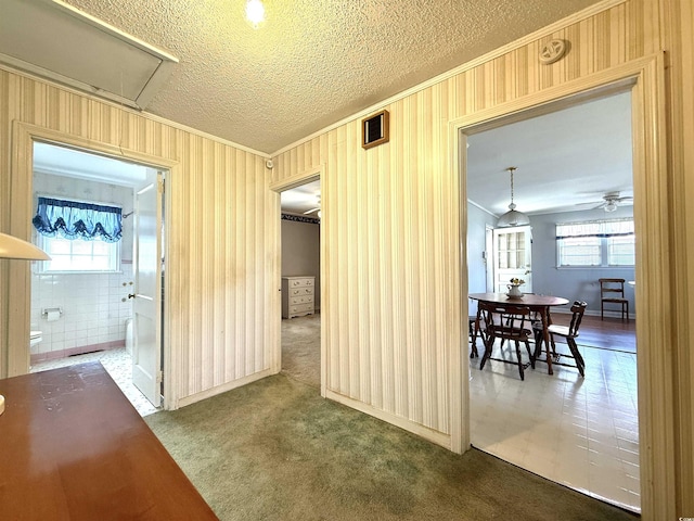 hall featuring a textured ceiling, ornamental molding, visible vents, carpet floors, and attic access