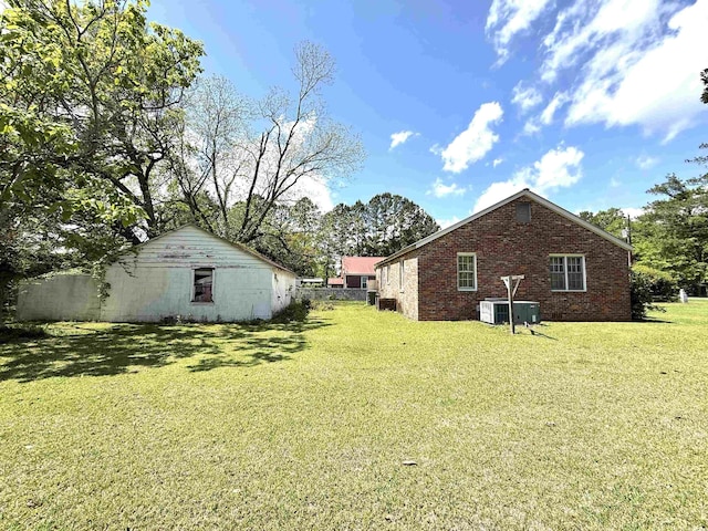 view of side of home featuring a yard, fence, an outdoor structure, central air condition unit, and brick siding