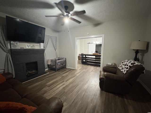 living area with ceiling fan with notable chandelier, a fireplace, wood finished floors, and a textured ceiling