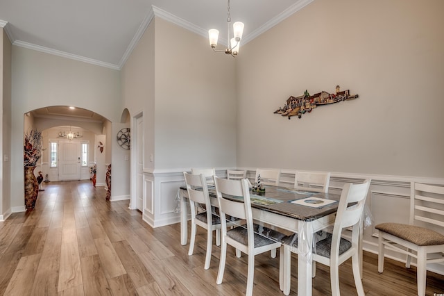 dining room with crown molding, arched walkways, a notable chandelier, and wainscoting