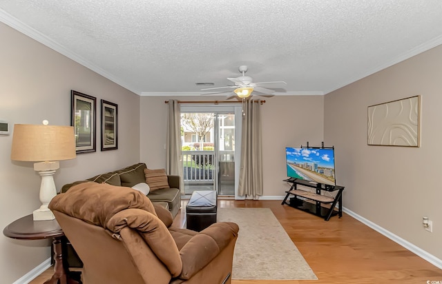 living room with crown molding, a textured ceiling, a ceiling fan, visible vents, and light wood finished floors