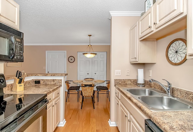 kitchen with light countertops, black appliances, decorative light fixtures, light wood finished floors, and a sink