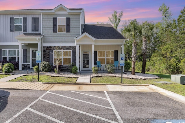 view of front of property featuring covered porch, a front yard, uncovered parking, and stone siding