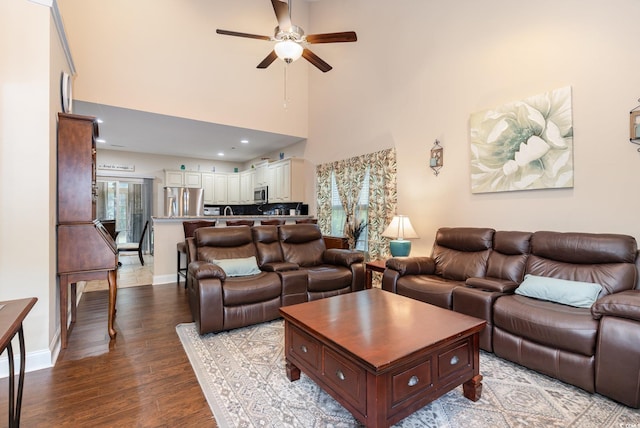 living room featuring baseboards, a towering ceiling, ceiling fan, and wood finished floors