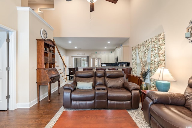 living area with stairs, ceiling fan, wood finished floors, and a towering ceiling