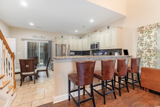 kitchen with a kitchen breakfast bar, backsplash, light stone counters, a peninsula, and stainless steel appliances