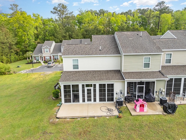 rear view of property with a yard, roof with shingles, a patio area, and a sunroom