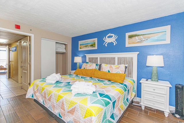 bedroom with wood tiled floors, a closet, a textured ceiling, and baseboards