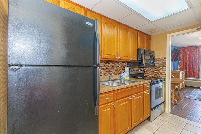 kitchen featuring black appliances, a sink, brown cabinetry, decorative backsplash, and light tile patterned floors