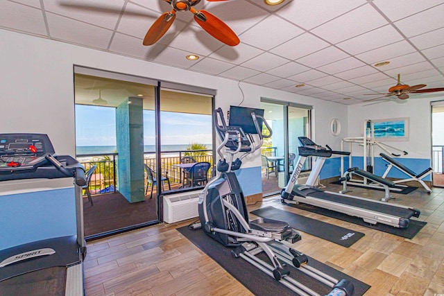 gym with a ceiling fan, wood finished floors, healthy amount of natural light, and a paneled ceiling