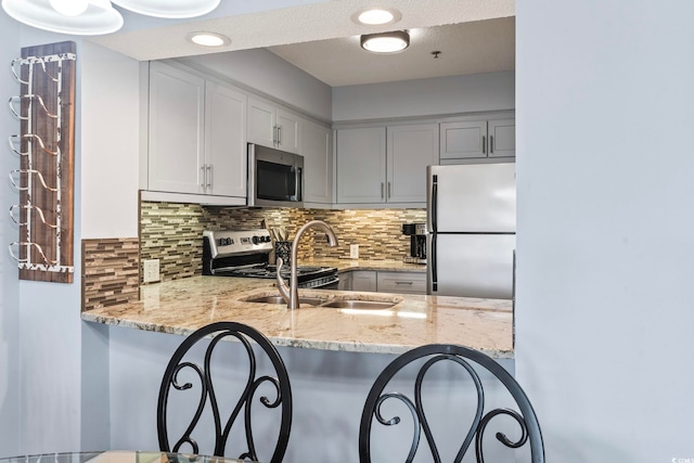 kitchen featuring stainless steel appliances, tasteful backsplash, light stone counters, a breakfast bar, and a peninsula