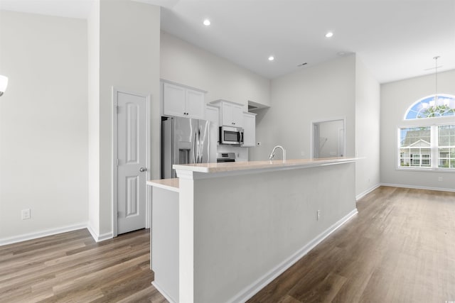 kitchen featuring appliances with stainless steel finishes, wood finished floors, light countertops, baseboards, and a high ceiling