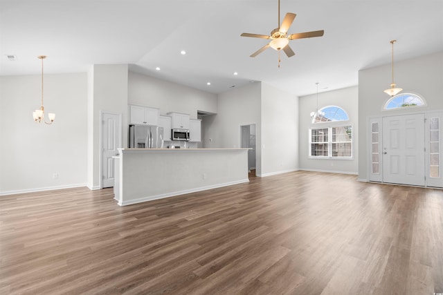 unfurnished living room featuring high vaulted ceiling, a chandelier, ceiling fan, light wood-type flooring, and baseboards