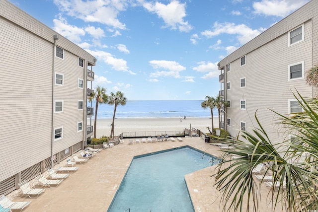 community pool with view of water and beach and a patio area