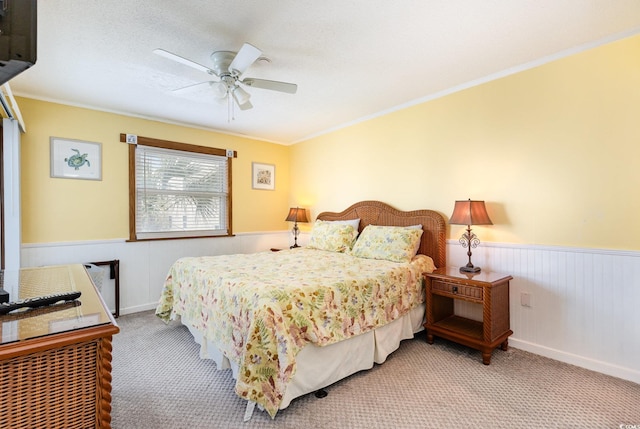 bedroom with carpet floors, wainscoting, ornamental molding, and a ceiling fan