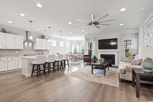living room featuring light wood-type flooring, recessed lighting, ceiling fan, and a glass covered fireplace