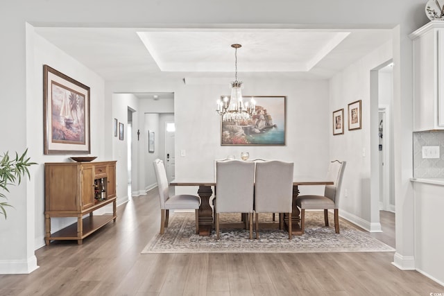 dining area featuring light wood-type flooring, an inviting chandelier, and a tray ceiling
