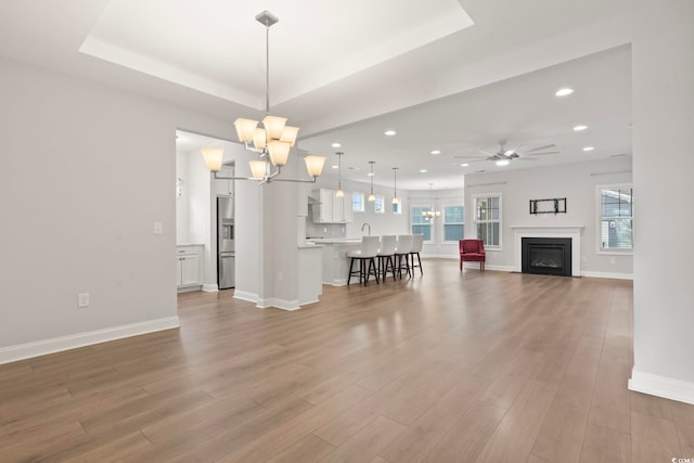 living area with recessed lighting, wood finished floors, a raised ceiling, and ceiling fan with notable chandelier