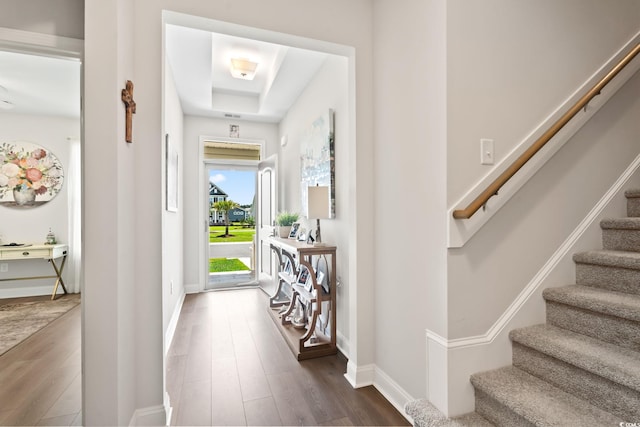 foyer entrance featuring baseboards, stairs, dark wood-style flooring, and a tray ceiling