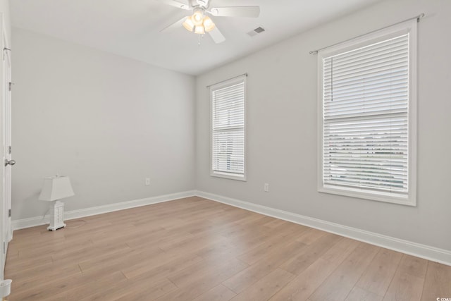 spare room featuring light wood-style floors, a ceiling fan, visible vents, and baseboards