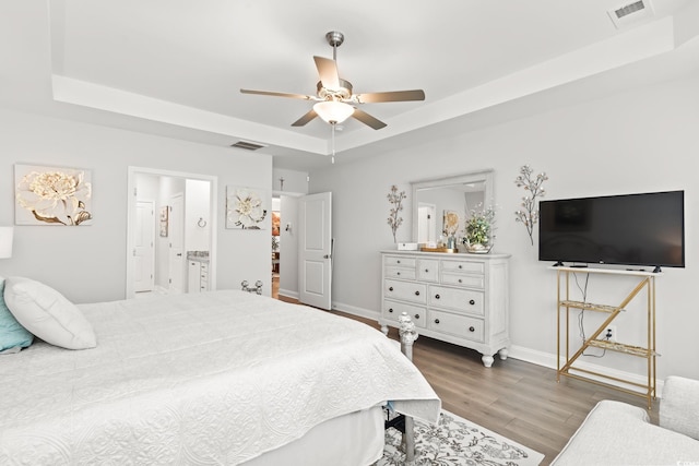 bedroom featuring wood finished floors, visible vents, a tray ceiling, and baseboards