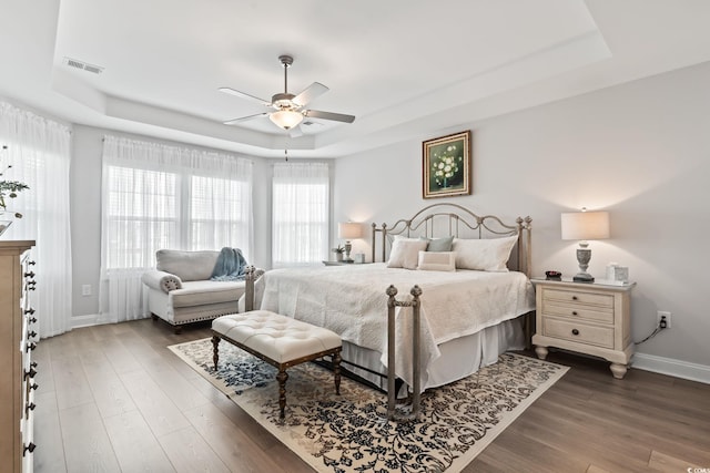 bedroom with baseboards, visible vents, a raised ceiling, and wood finished floors