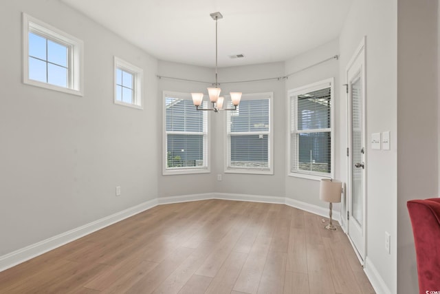 unfurnished dining area with light wood-style flooring, a chandelier, visible vents, and baseboards