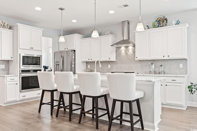 kitchen with white cabinetry, stainless steel appliances, wall chimney range hood, and decorative backsplash