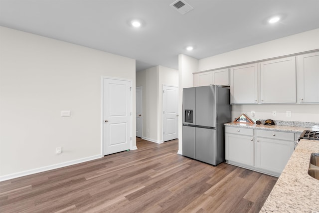 kitchen with stainless steel refrigerator with ice dispenser, light wood finished floors, light stone counters, baseboards, and recessed lighting
