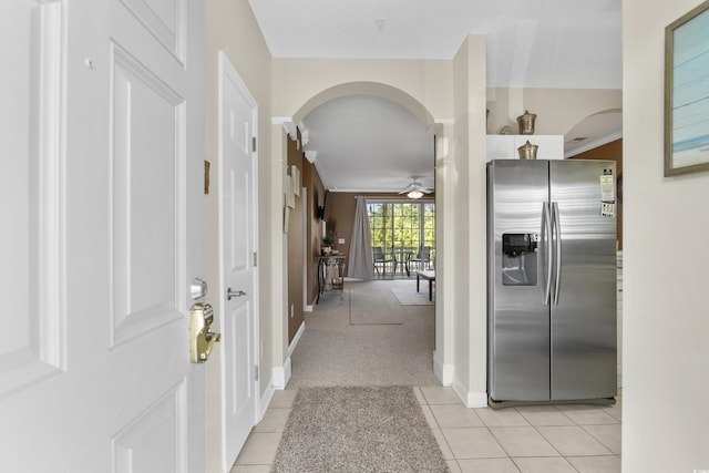 hallway featuring arched walkways, baseboards, light carpet, and light tile patterned floors