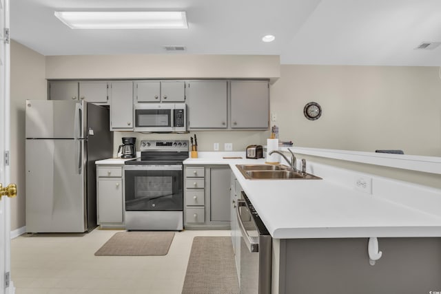 kitchen featuring gray cabinetry, appliances with stainless steel finishes, a peninsula, and a sink