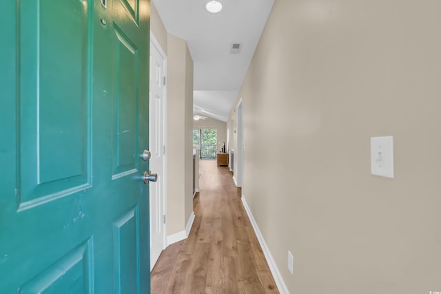 hall featuring baseboards, vaulted ceiling, light wood finished floors, and visible vents