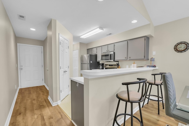 kitchen featuring light wood-type flooring, gray cabinetry, light countertops, a peninsula, and stainless steel appliances