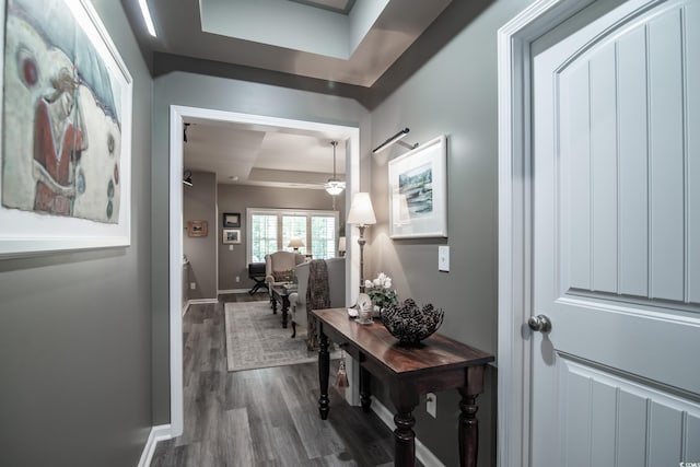 hallway featuring a raised ceiling, dark wood finished floors, and baseboards