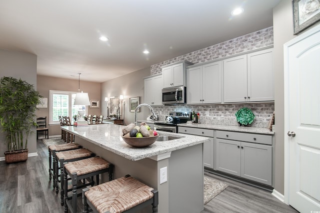 kitchen with tasteful backsplash, wood finished floors, stainless steel appliances, a kitchen bar, and a center island with sink