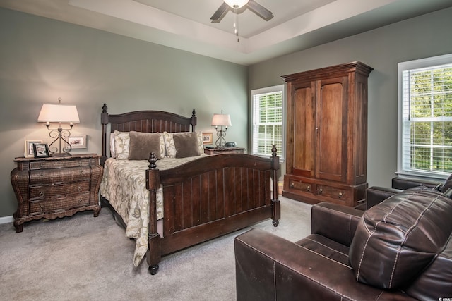 bedroom featuring a raised ceiling, ceiling fan, and light carpet