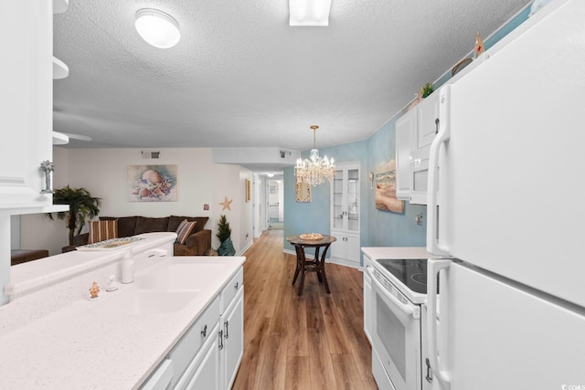 kitchen with a notable chandelier, white cabinetry, white appliances, and light countertops