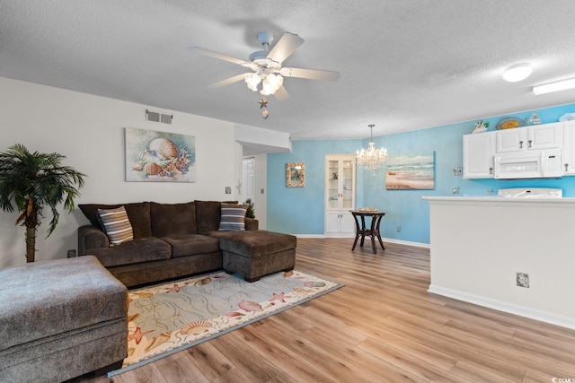 living room featuring visible vents, light wood-type flooring, baseboards, a textured ceiling, and ceiling fan with notable chandelier