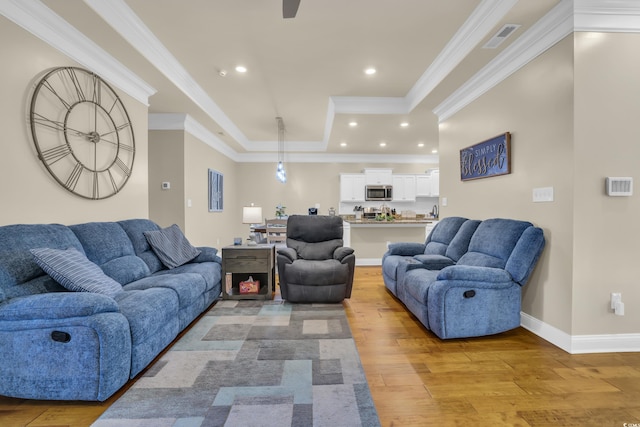 living room with light wood-style flooring, recessed lighting, a tray ceiling, visible vents, and ornamental molding