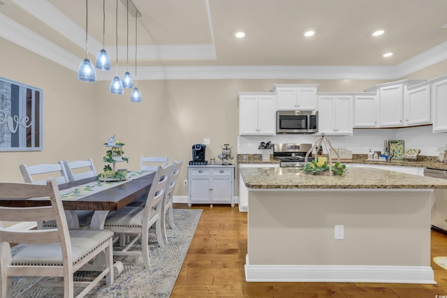 kitchen featuring a center island with sink, ornamental molding, stainless steel appliances, and white cabinetry