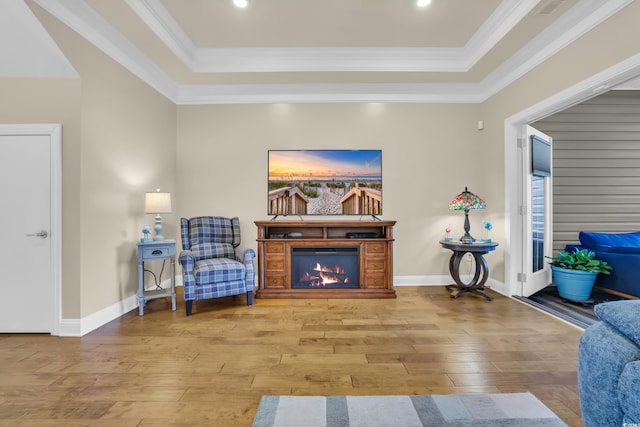 sitting room with crown molding, a lit fireplace, a tray ceiling, and hardwood / wood-style floors