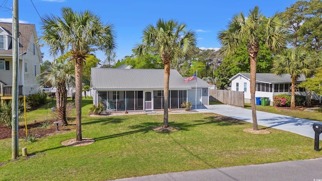 view of front of property featuring a front lawn, fence, a sunroom, metal roof, and driveway