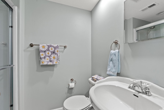 bathroom with a sink, toilet, baseboards, a shower with door, and visible vents
