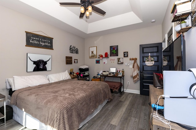 bedroom featuring baseboards, a tray ceiling, ceiling fan, and wood finished floors
