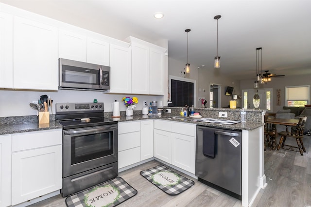 kitchen featuring a sink, a peninsula, open floor plan, stainless steel appliances, and light wood-style flooring