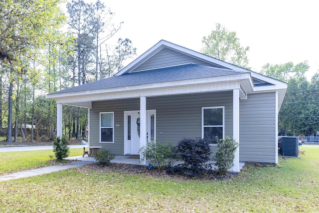 bungalow-style home with a porch, central AC unit, a front lawn, and roof with shingles