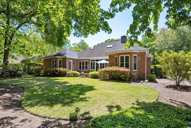 rear view of property featuring brick siding, a chimney, and a lawn
