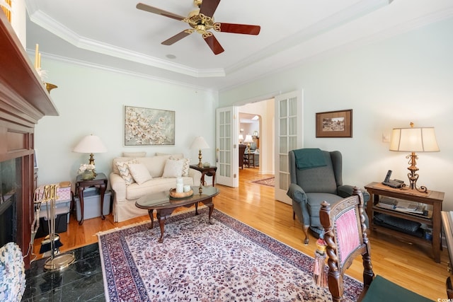 living room with ornamental molding, ceiling fan, a tray ceiling, and a high end fireplace