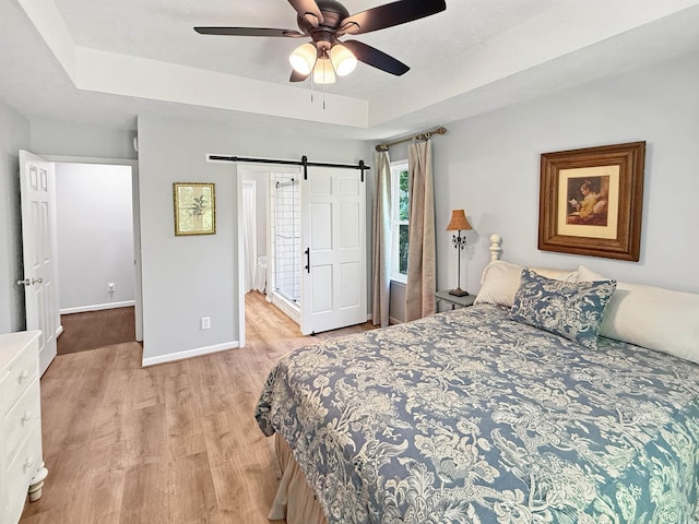 bedroom featuring a barn door, light wood-style floors, baseboards, and a raised ceiling